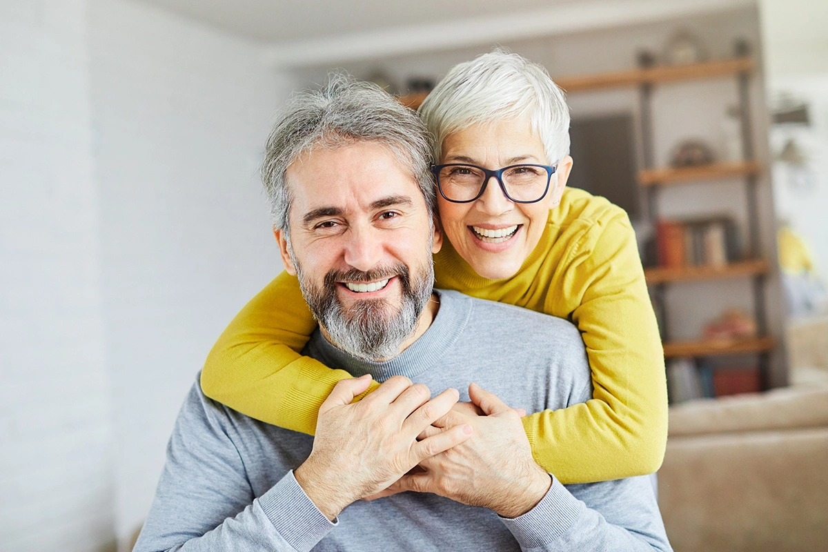 Happy older couple embracing in bright home interior, smiling warmly together.