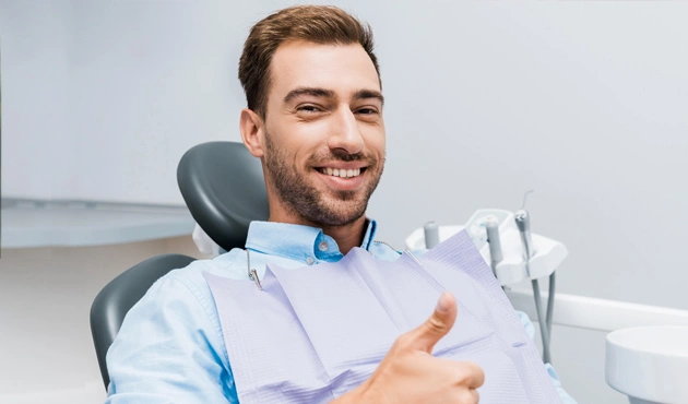 Smiling male patient in dental chair giving thumbs up in modern dental office setting.