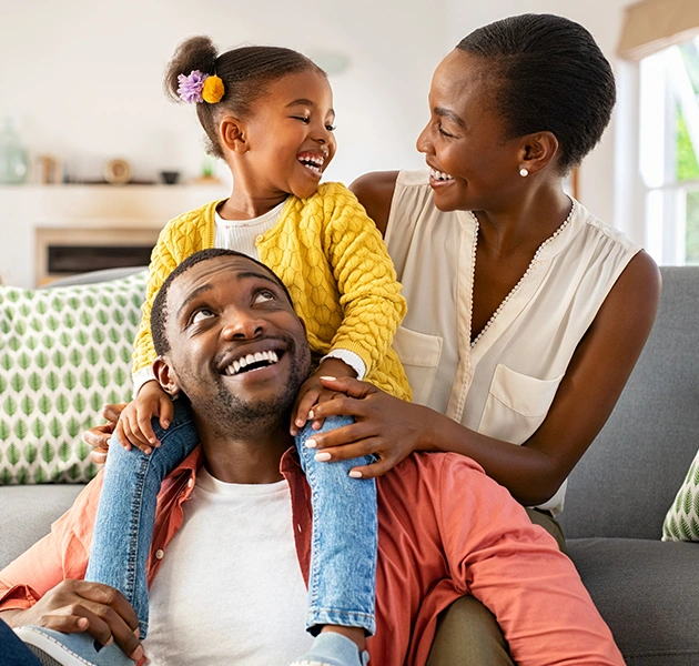 Happy family with young daughter sitting together on couch at home, smiling.