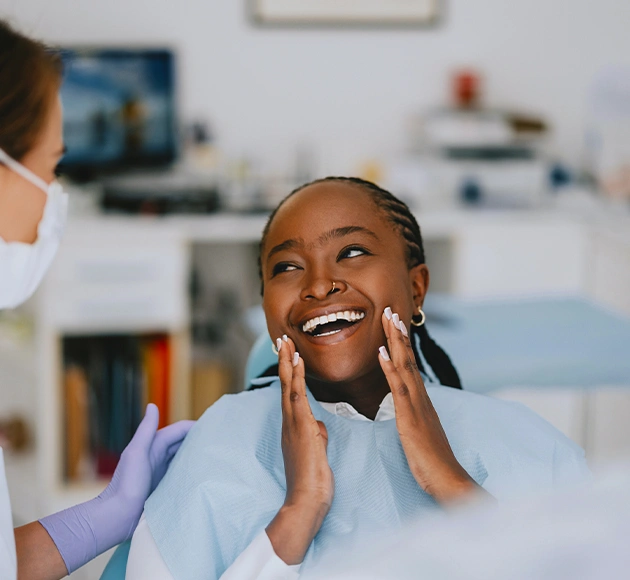 Young woman smiling with hands to face in modern dental office setting.