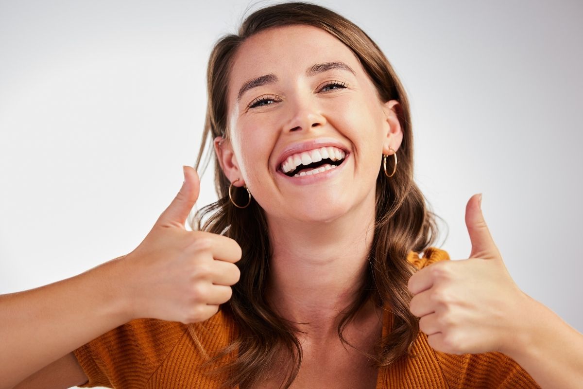 Smiling woman showing two thumbs up, symbolizing comfort and positive results following a dental procedure