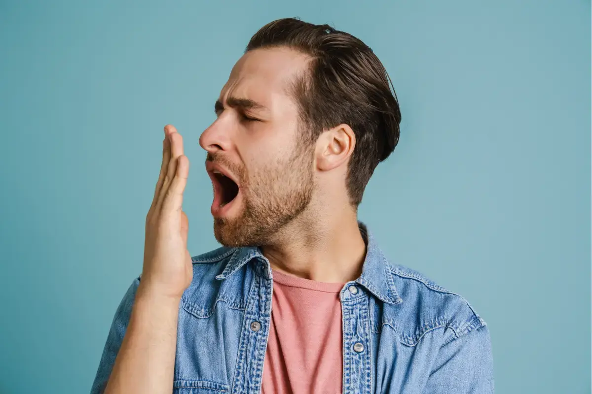 Man checking his breath with hand near mouth against blue background.